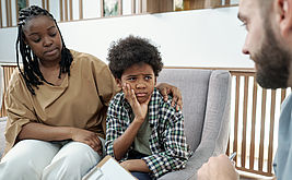 Mutter und skeptischer Sohn blicken zum Therapeuten