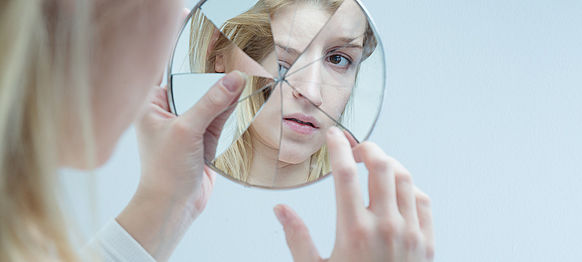 Frau betrachtet sich in zerbrochenem Spiegel