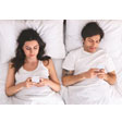 Mann und Frau nebeneinander im Bett liegend, beide mit Smartphone in der Hand