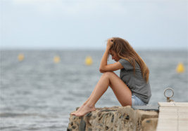 Mädchen sitzt allein und traurig am Wasser