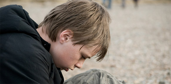 Junge mit schwarzer Jacke kauert traurig am Boden