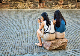 Zwei Frauen auf Stein sitzend, beide mit Smartphone in der Hand