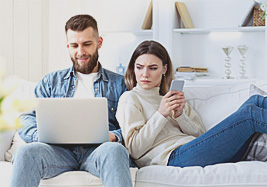 Paar auf Sofa, Mann mit Laptop, Frau mit Smartphone